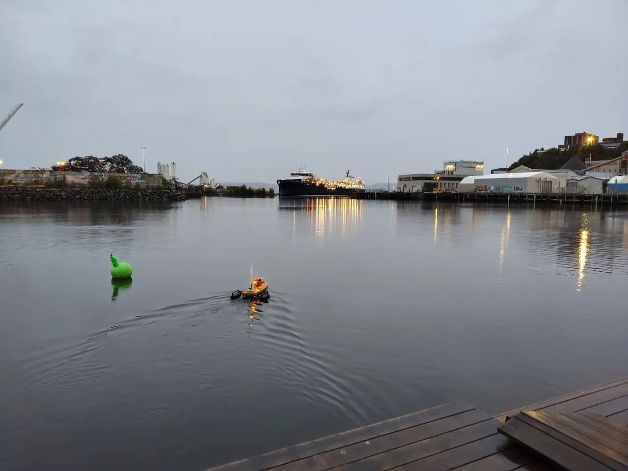 Autonomous surface vehicle navigating a harbour at dusk with a green buoy nearby
