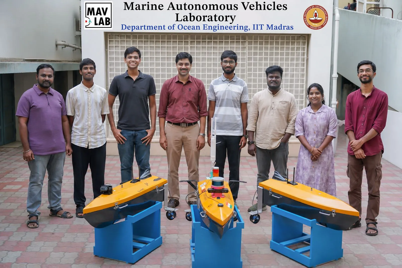 MAV Lab members with three yellow and black autonomous surface vehicles on blue stands